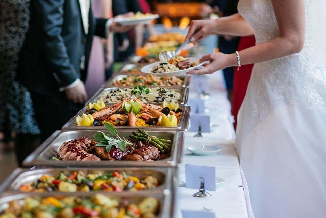 Bruiloftsbuffet met warme gerechten, een bruid schept haar bord op